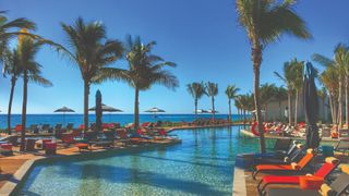 Swimming pool lined with red sunbeds and palm trees at Andaz Mayakoba Resort Riviera Maya