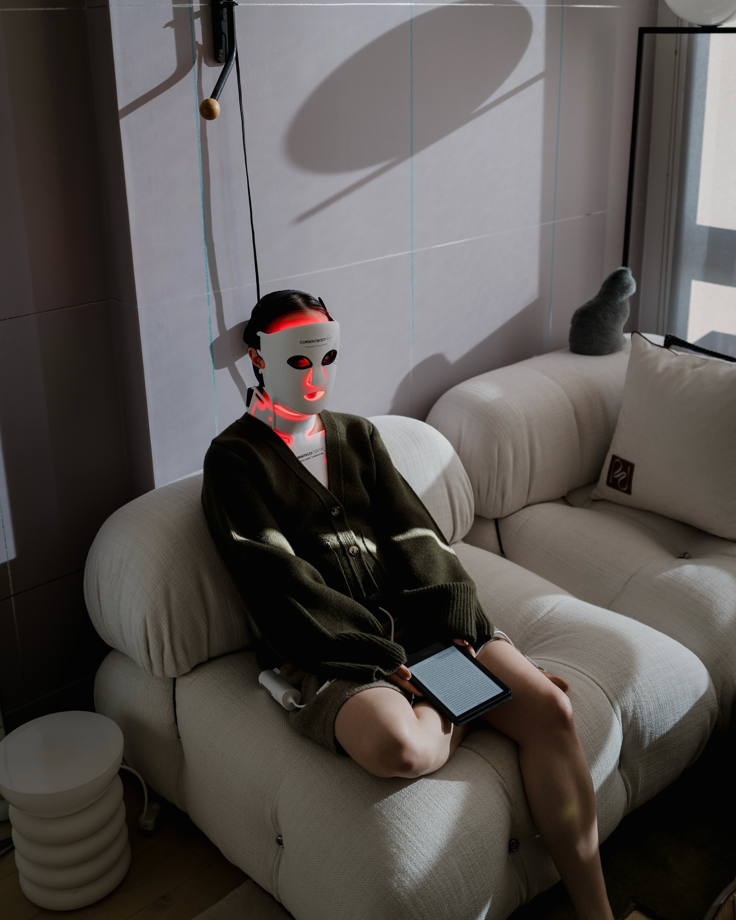 A woman sitting on a sofa wearing an LED mask