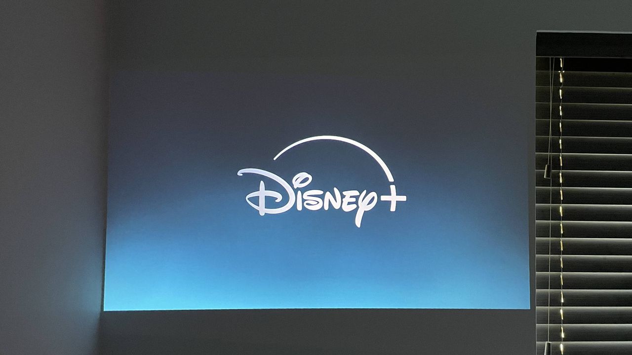 The Disney Plus app title page is projected onto a wall next to a window with the blinds closed.