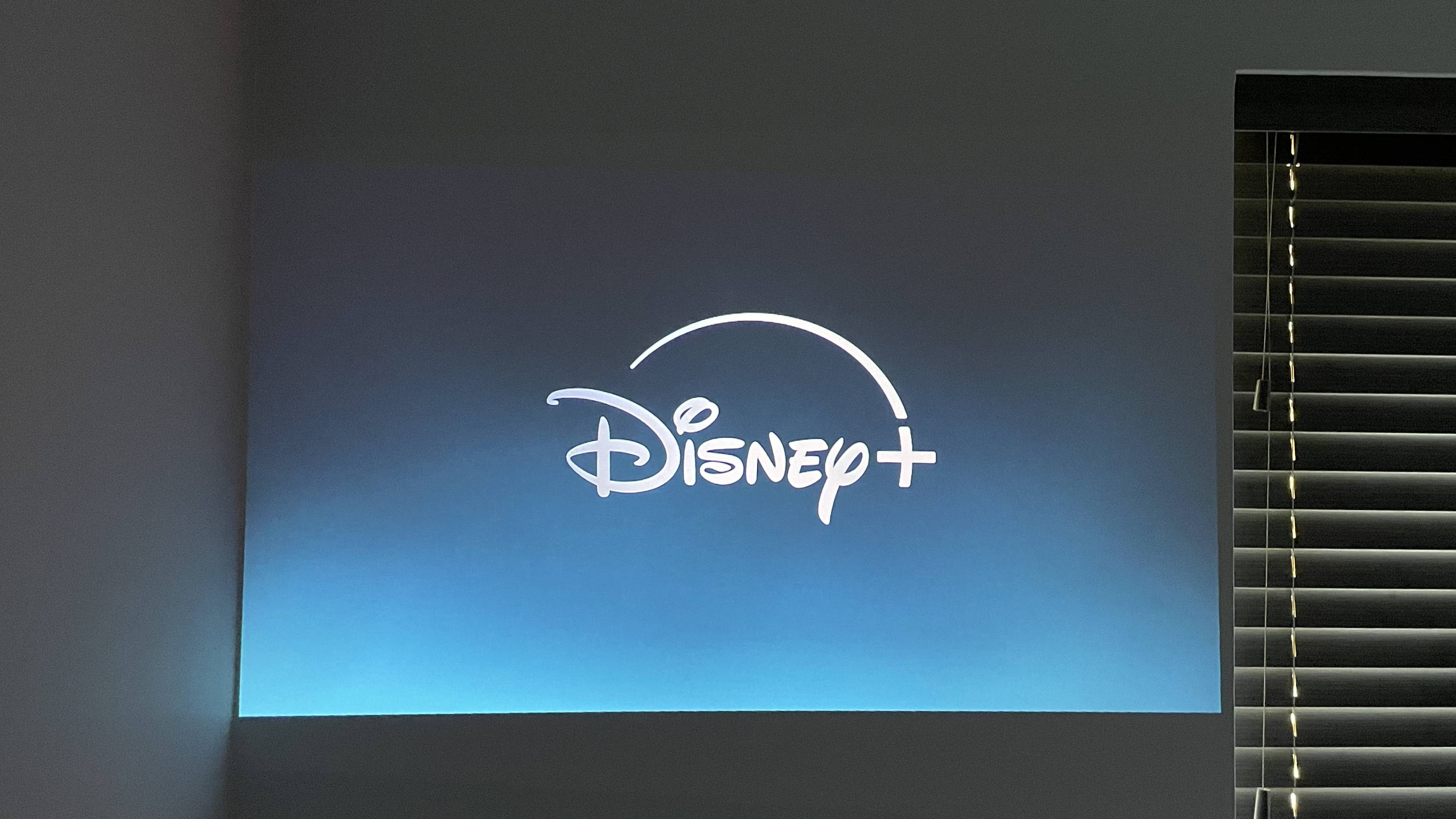The Disney Plus app title page is projected onto a wall next to a window with the blinds closed.