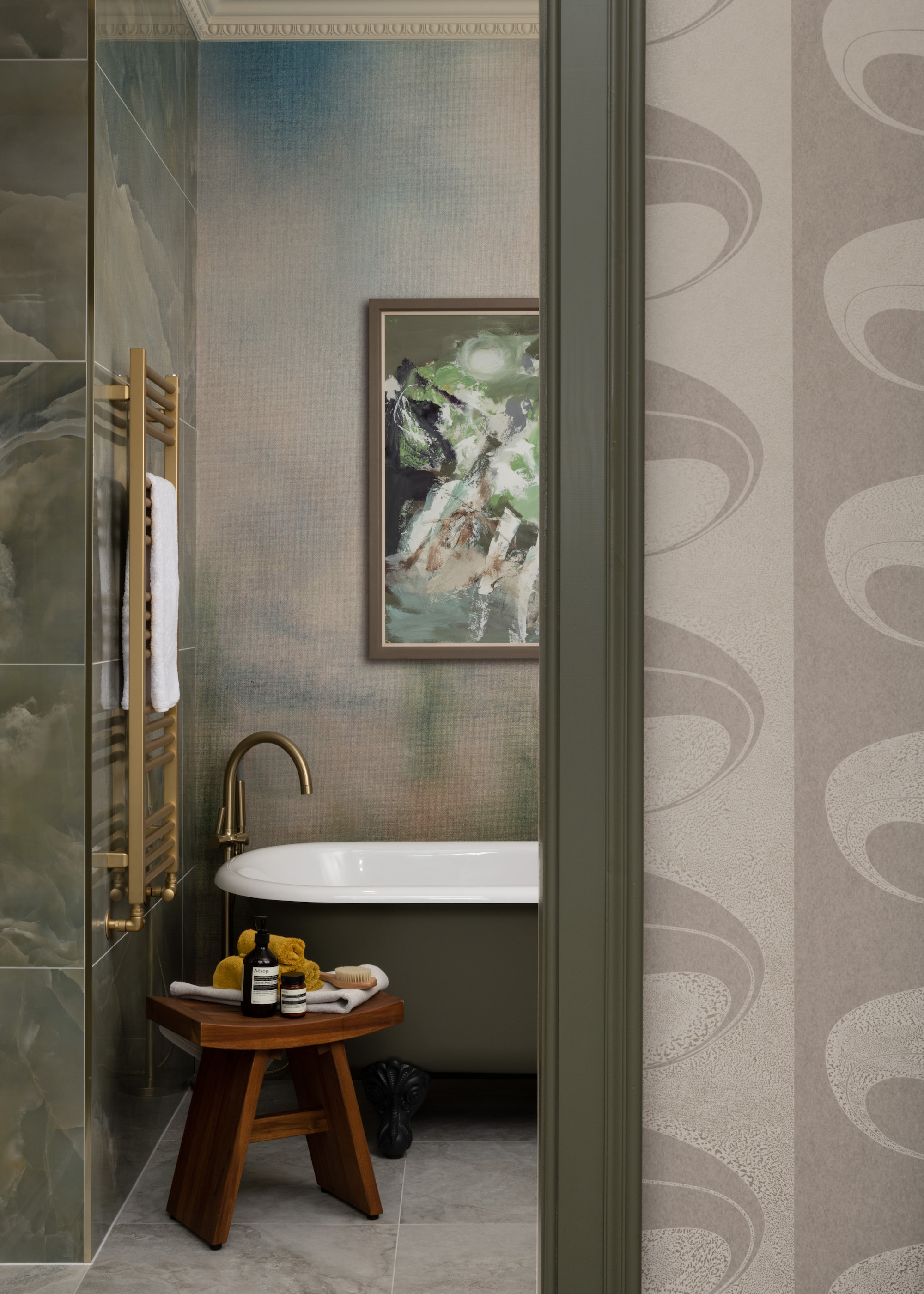 small ensuite bathroom with green bath and wooden stool and artwork