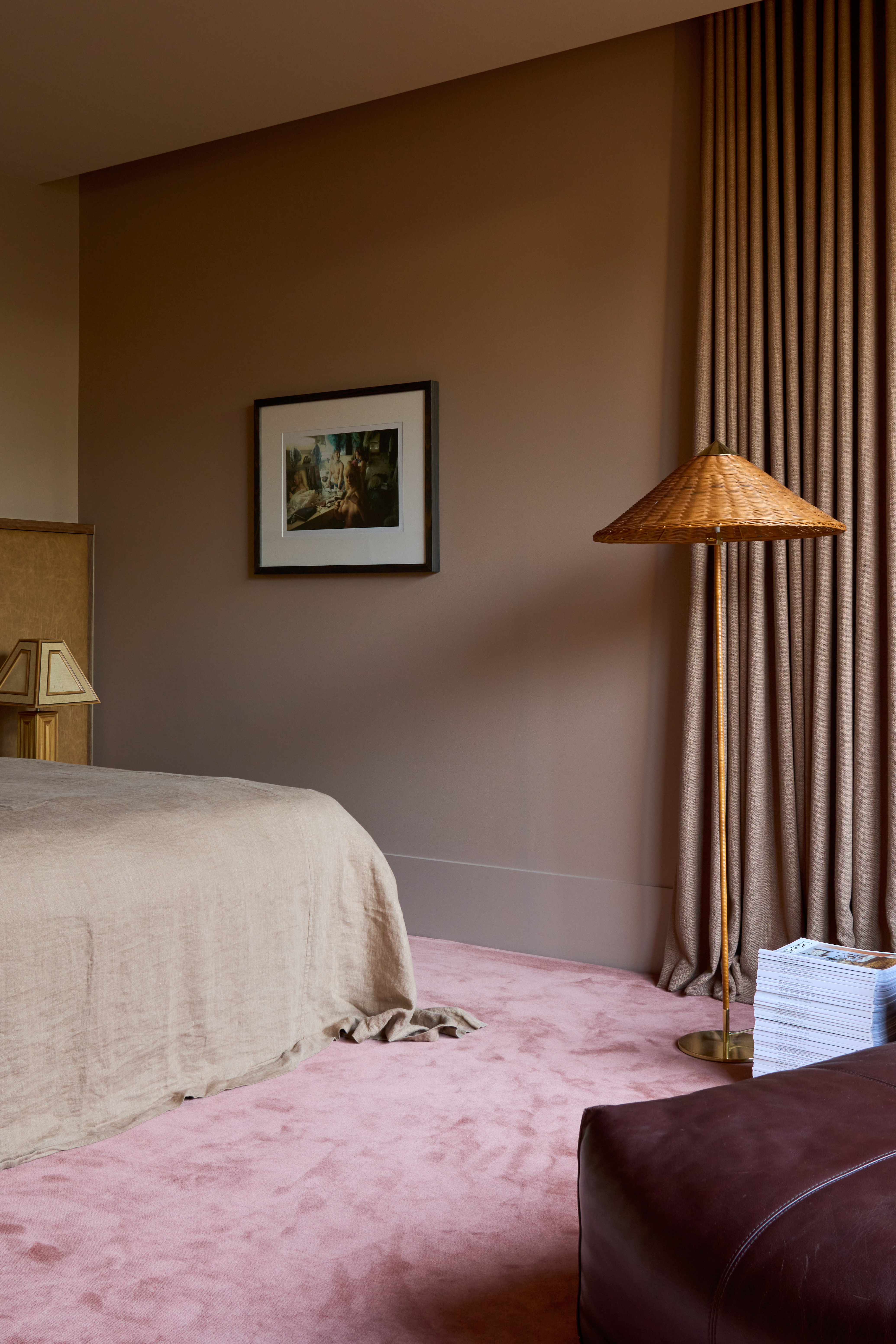 A bedroom with pink carpet with brown walls and a wicker floor lamp