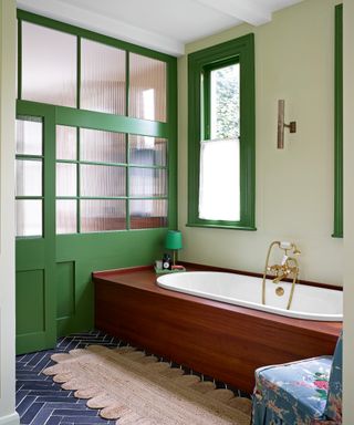 bathroom with pale walls, green doors and windows, and bath with wooden surround