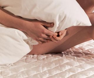 A woman holding a pillow sitting on the Sijo TempTune Cooling Mattress Pad.