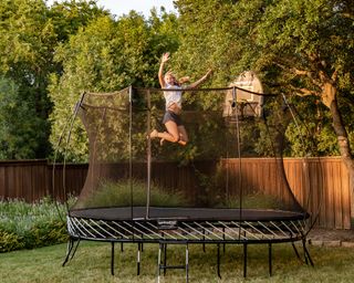 girl jumping on a large circular trampoline with an enclosure