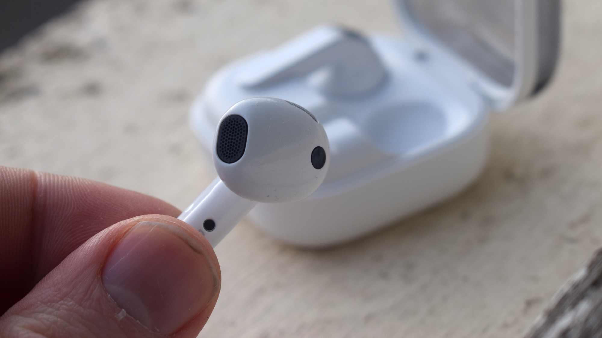 The Samsung Galaxy Buds 4 earbuds in a man's hand, with the case behind.