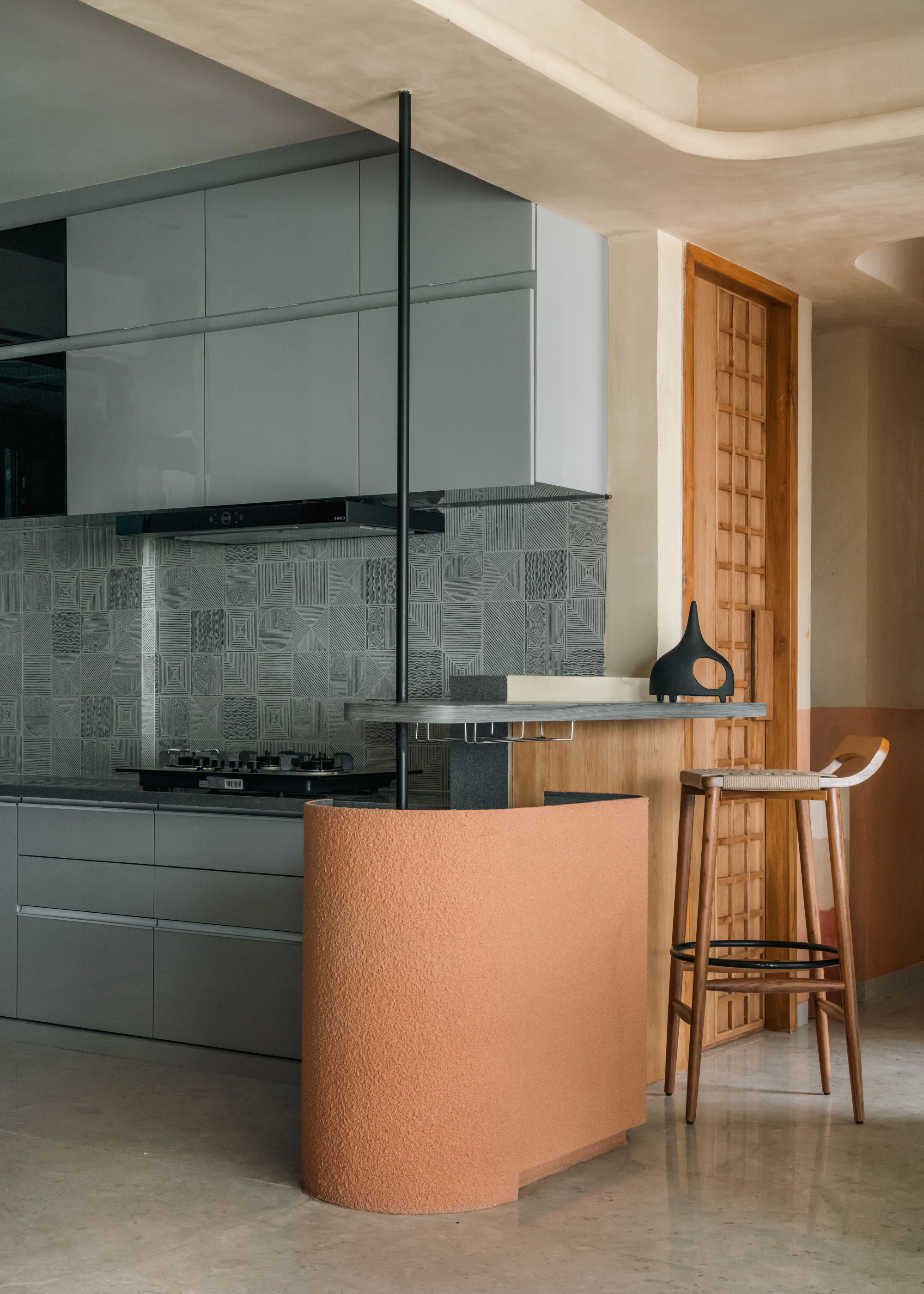 An airy kitchen with pale blue cabinets and drawers, blue tiled backsplash, a stove, and an extended table with a terracotta textured base beside a wood stool