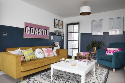Blue living room with monochrome Scandi rug, white coffee table, yellow sofa, teal armchair and large 'Coastie' pink print