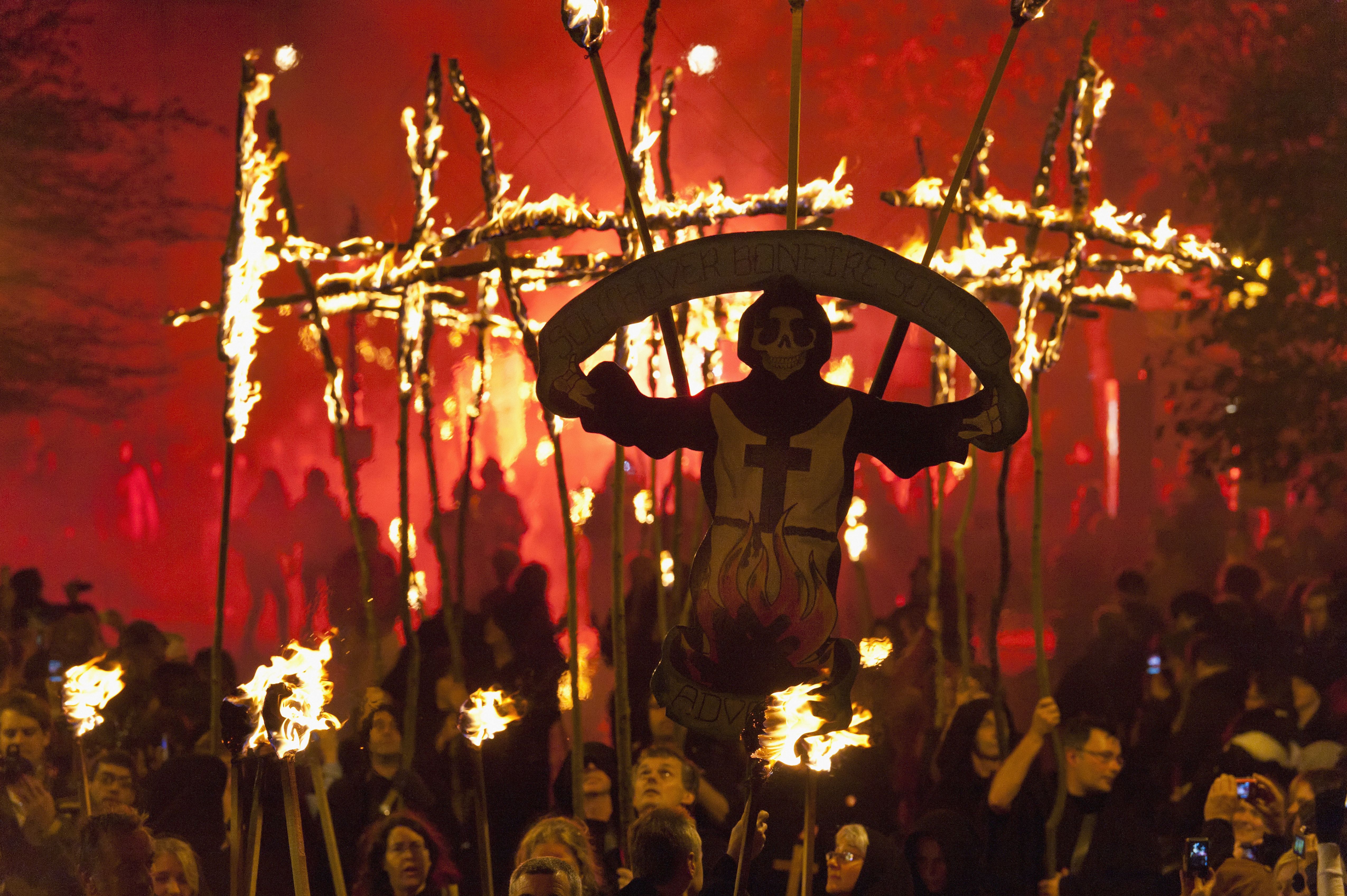People Dressed As Monks Carrying Southover Bonfire Society Banner And Burning Crosses Lit From Behind By Red Flare On Bonfire Night