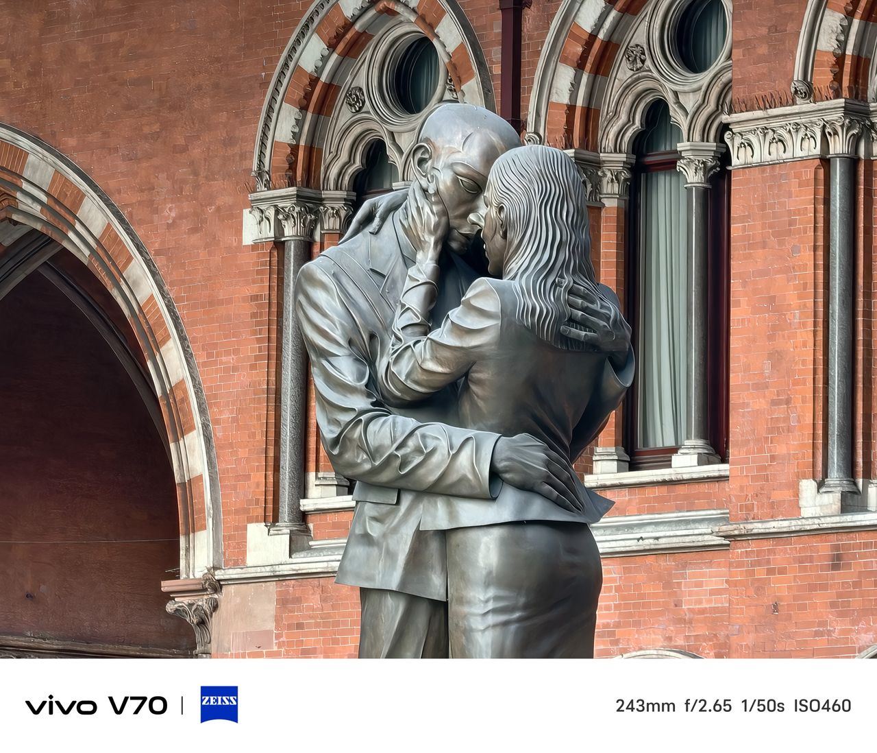 Close-up of bronze &ldquo;The Meeting Place&rdquo; statue of embracing couple against red-brick backdrop.