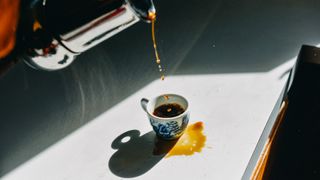 coffee being poured and spilled into a small mug on a white surface