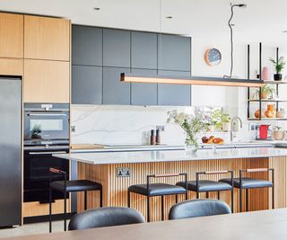 A new kitchen flooded with natural light. There is a mixture of dark and natural wood cabinets and the central island has four bar stools seated at it