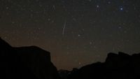 a streak of light zooms through the sky in front of background stars