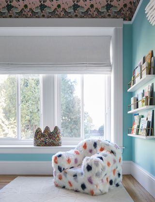 Children's bedroom with blue walls, wooden floor, book shelves and fluffy chair