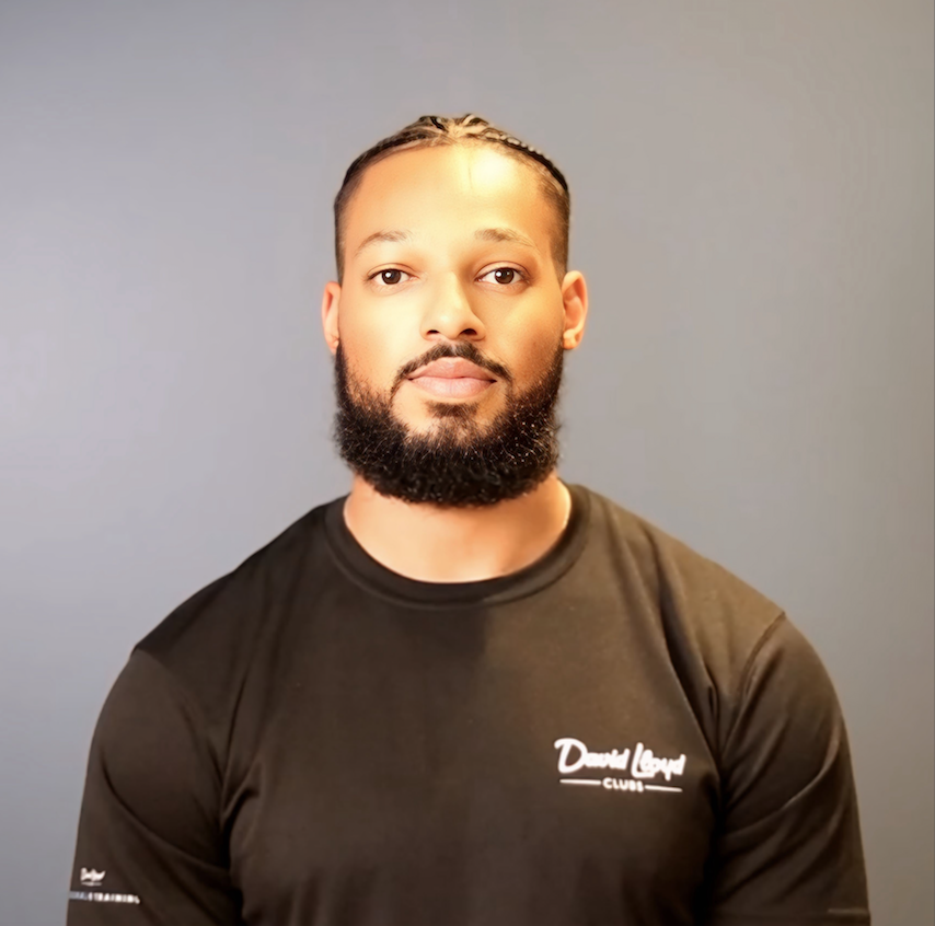 man looking at the camera from chest height wearing a black sleeved top with a plain grey background