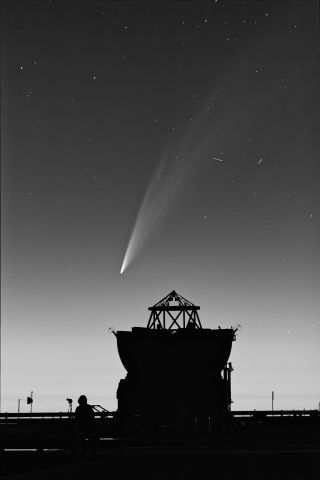 A black-and-white image taken in Chile depicting Comet G3 (ATLAS) 'wagging its tail' with part of the Paranal Observatory in the foreground