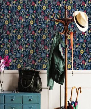 A small entryway with floral wallpaper, a coat stand, and blue drawers