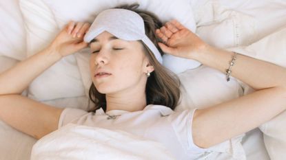 Woman sleeping on her back adjusting her sleep mask, sleep & wellness tips