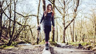 Young woman walking along fallen tree trunk in forest - another habits for happiness idea