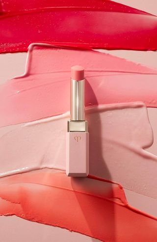 A pink-hued lip stick lays against a background covered in red, pink, fucsia, and poppy-red paint.