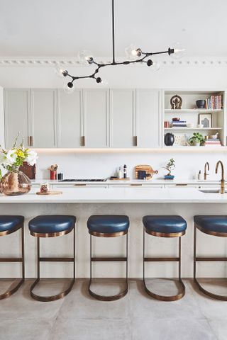 Black statement light in a white scheme with a row of blue and metal bar stools