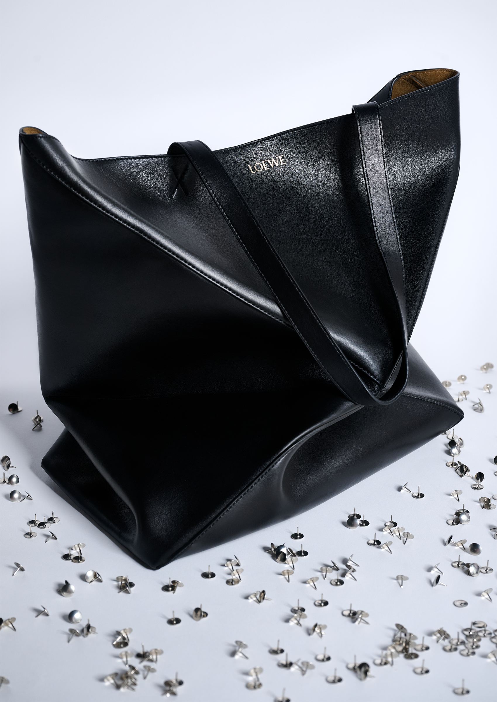 A black Loewe tote bag on a white table surrounded by silver thumbtacks