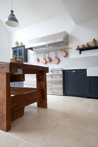 A blue kitchen with a wooden kitchen island and large, stone effect kitchen floor tiles