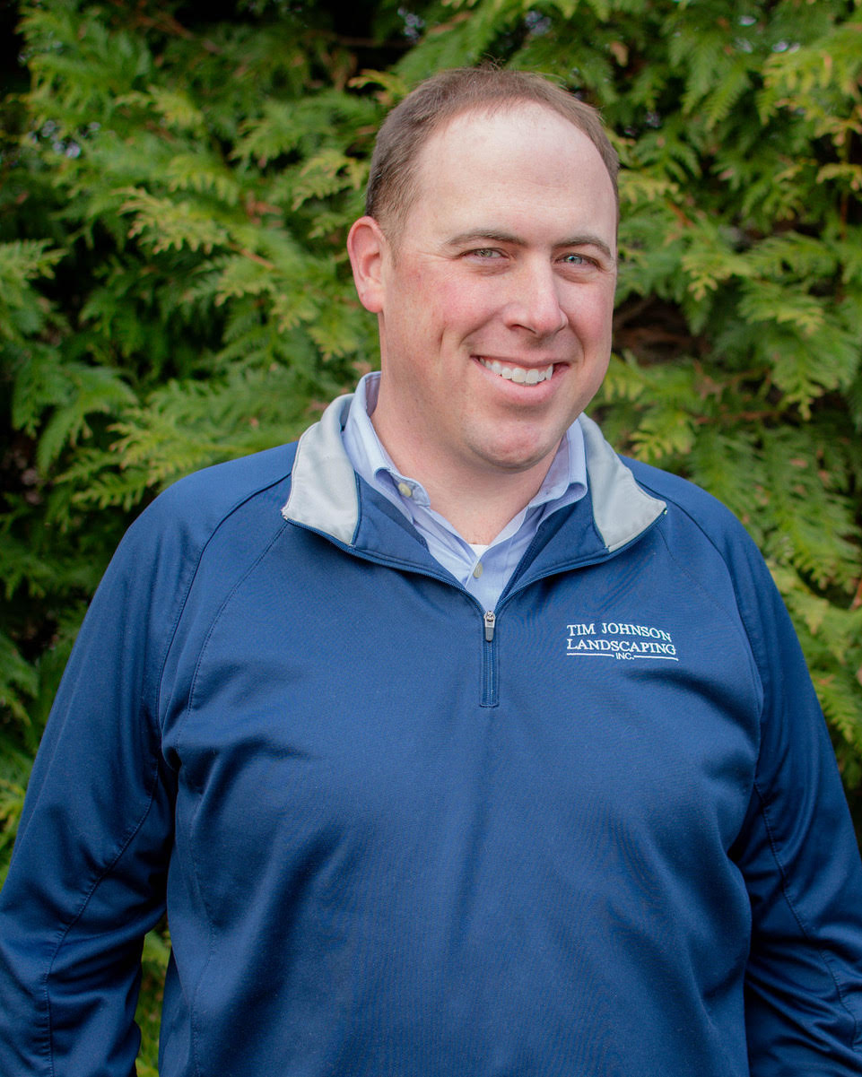Man stood in front of conifer in blue top