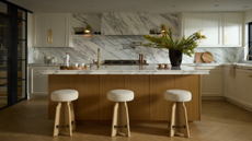 a beautiful marble kitchen with a detailed counter edge design, three stools and a marble splash back