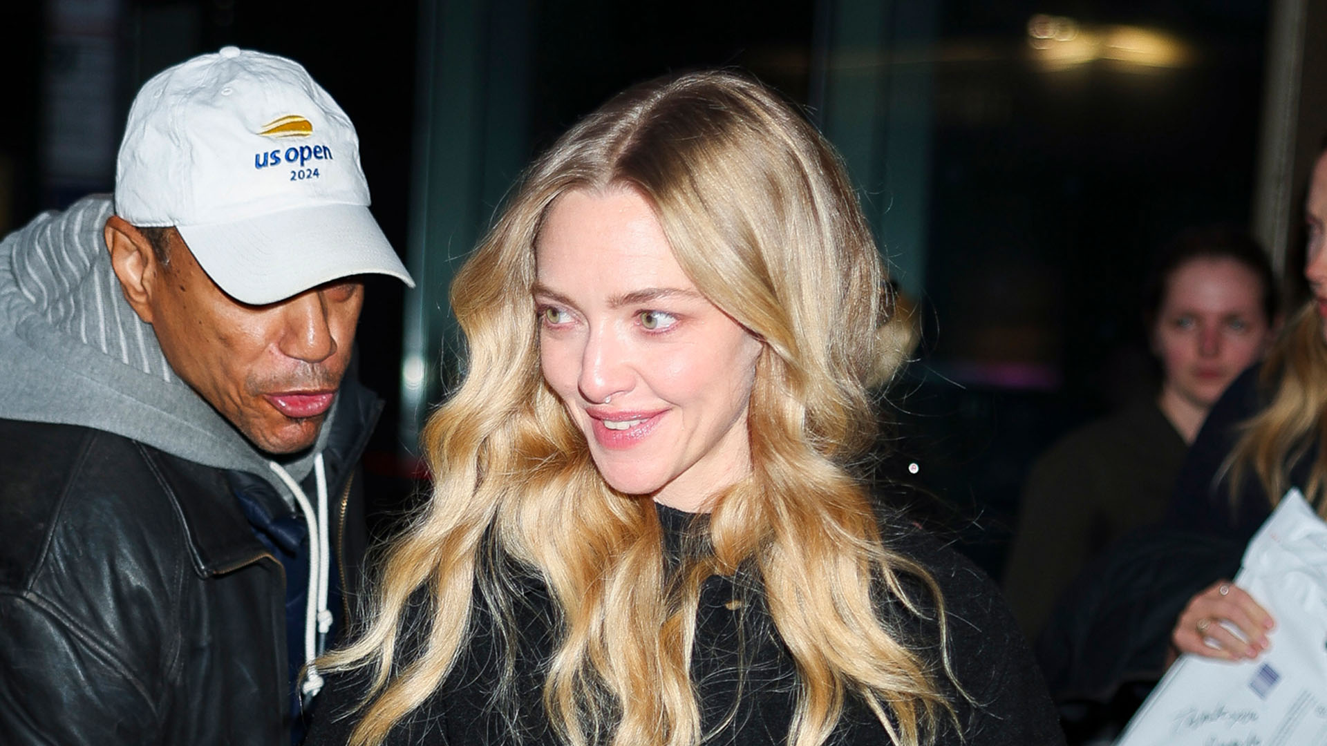 Amanda Seyfried wearing a black shacket, blue jeans, black boots, and a black woven bag