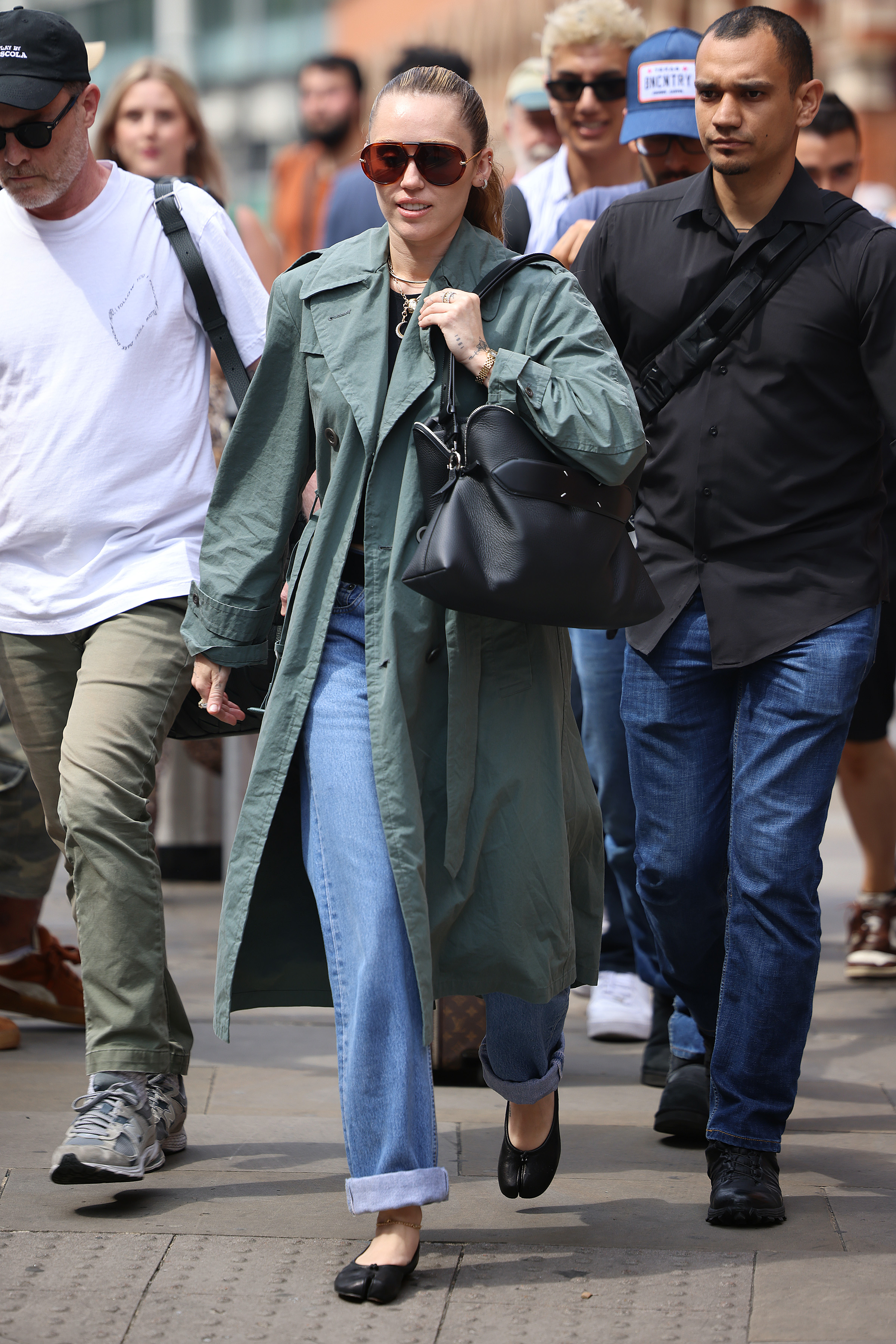 Miley Cyrus wearing a green trench coat, blue jeans, and black flats in London