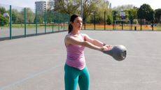 A woman performing a kettlebell swing at the park as part of a kettlebell workout