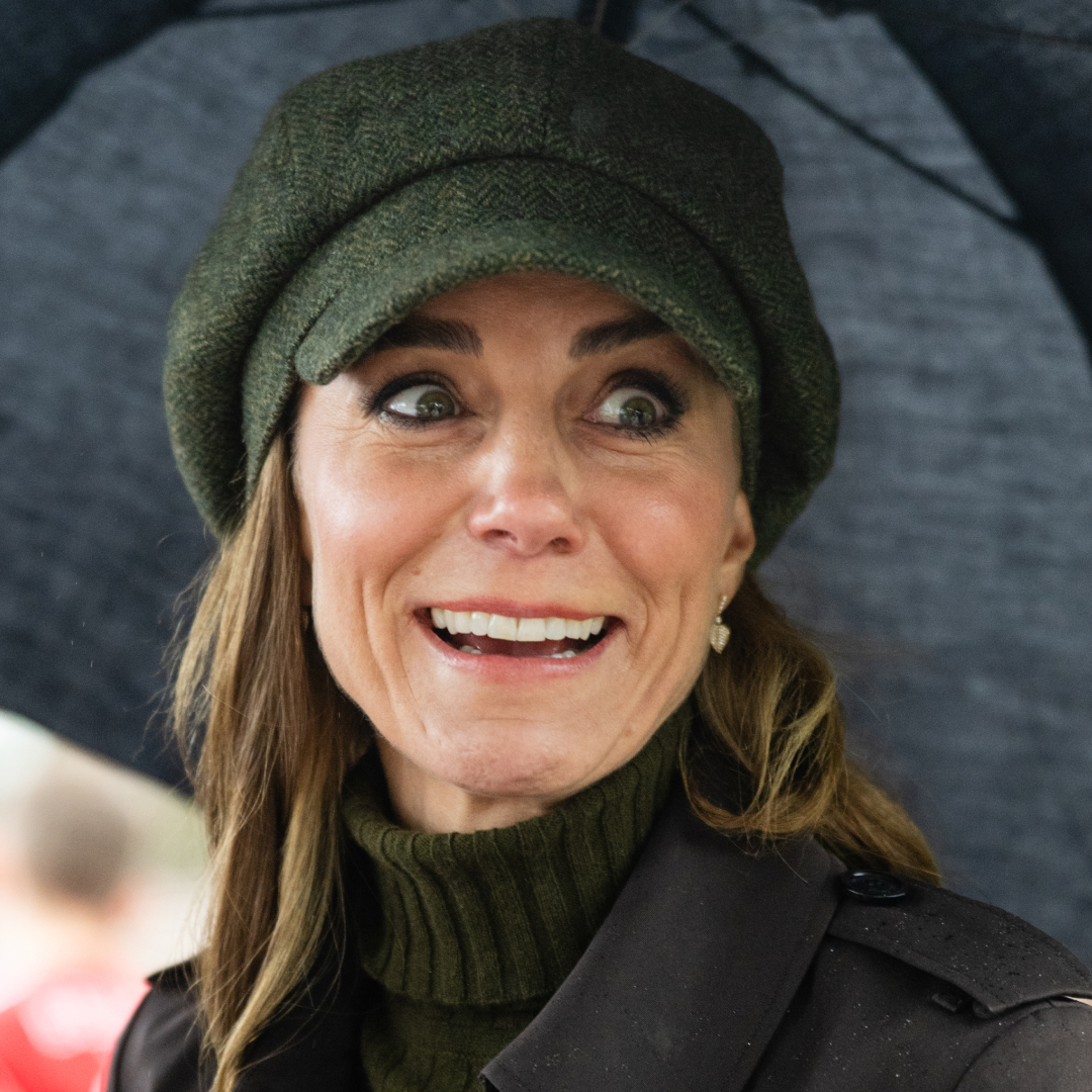 Princess Kate wearing a green cap holding an umbrella and grimacing