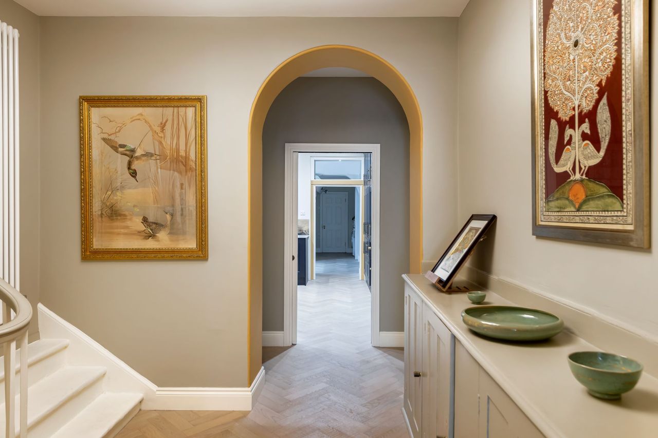 A hallway wityh curved doorways and herringbone wooden floor and a sideboard to the right of the image