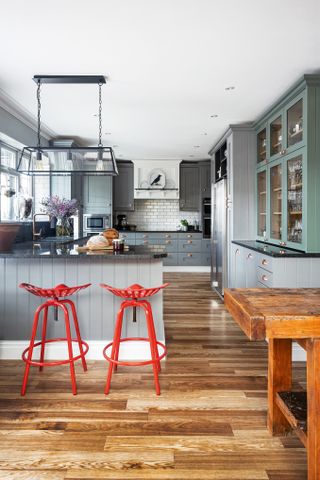 A grey kitchen with green cabinets and breakfast bar with red backless bar stools