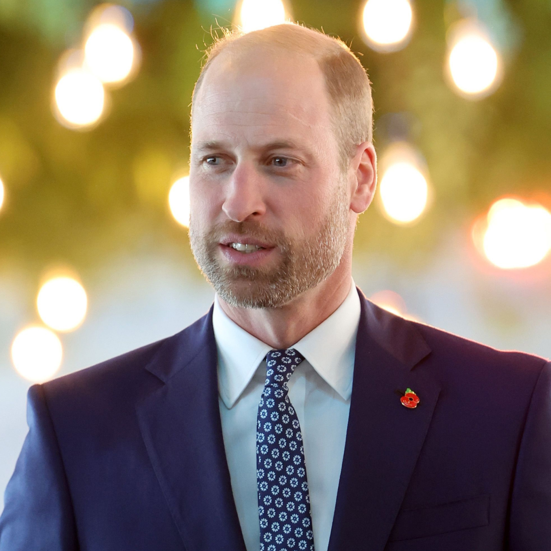 Prince William has a short beard and a bald head and wears a navy suit with a light blue shirt and a patterned tie