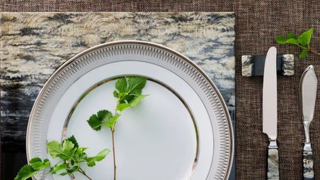 table setting with two stacked plates with foliage on it, a placemat, a knife resting on a cutlery rest, and another bread knife beside it