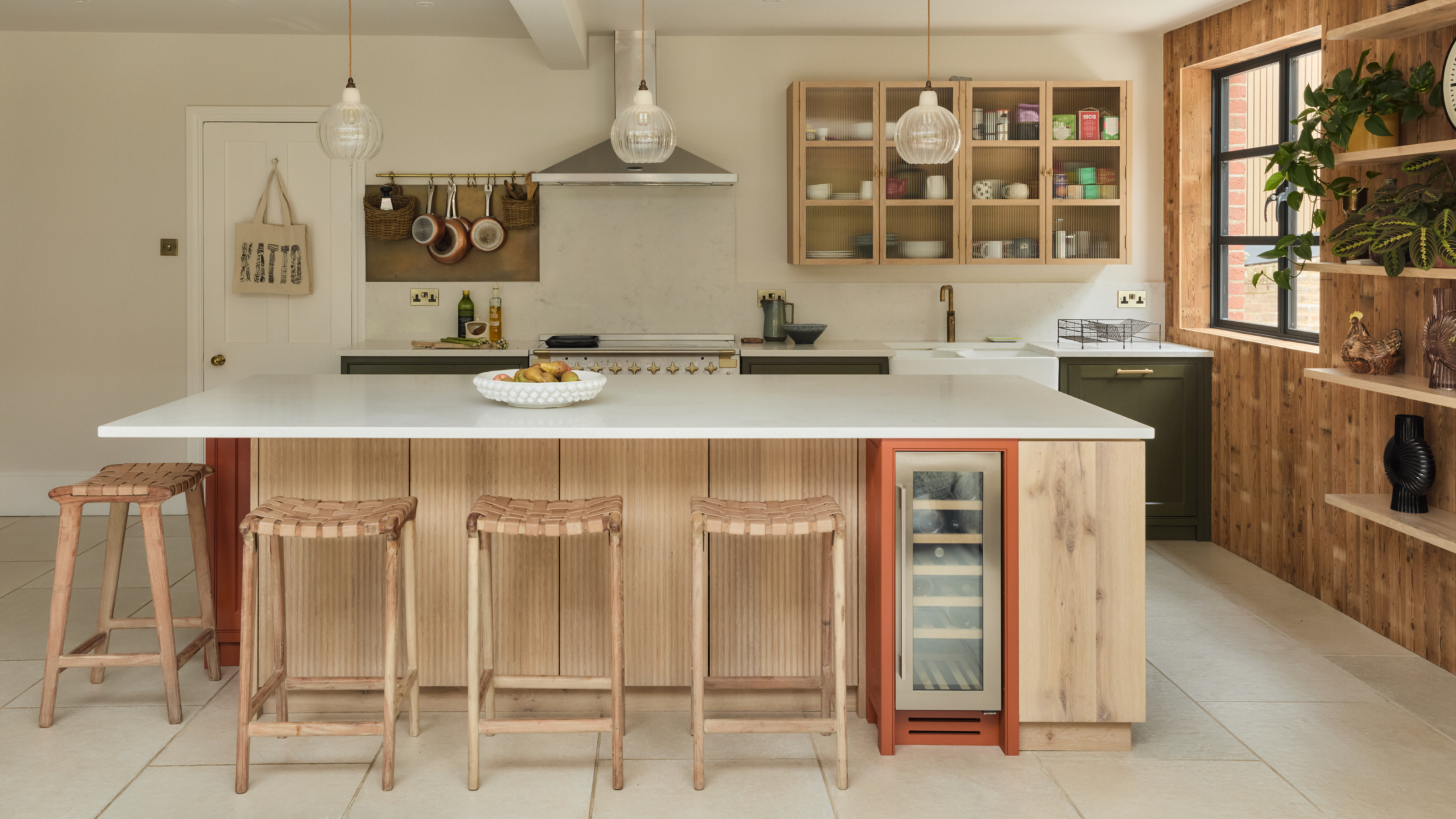 Rustic style kitchen with wood panelling on island and side wall, white worktops, wall cabinet storage, glass pendant lights, hanging saucepan rail, bar stools, wine fridge
