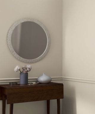 neutral walls in corner of room with wooden table, round mirror and flowers in vase