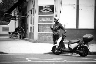 Image of a delivery driver standing next to his scooter, in black-and-white, taken on the Sigma 18-50mm f/2.8 DC DN | C Canon RF