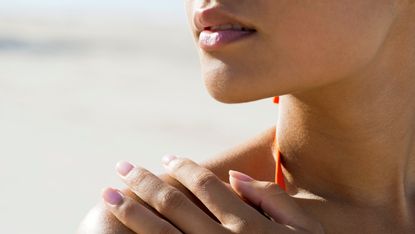 summer skincare main image of woman on the beach in swimsuit touching sun-exposed shoulders