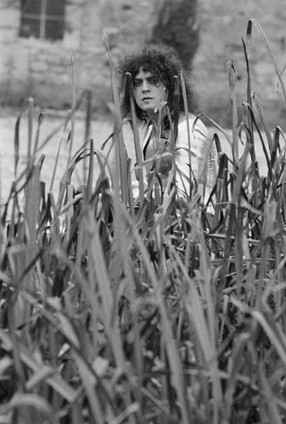 Marc Bolan sitting in a field of tall grass