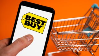 image of a phone with a best buy logo display and a shopping cart on orange background 