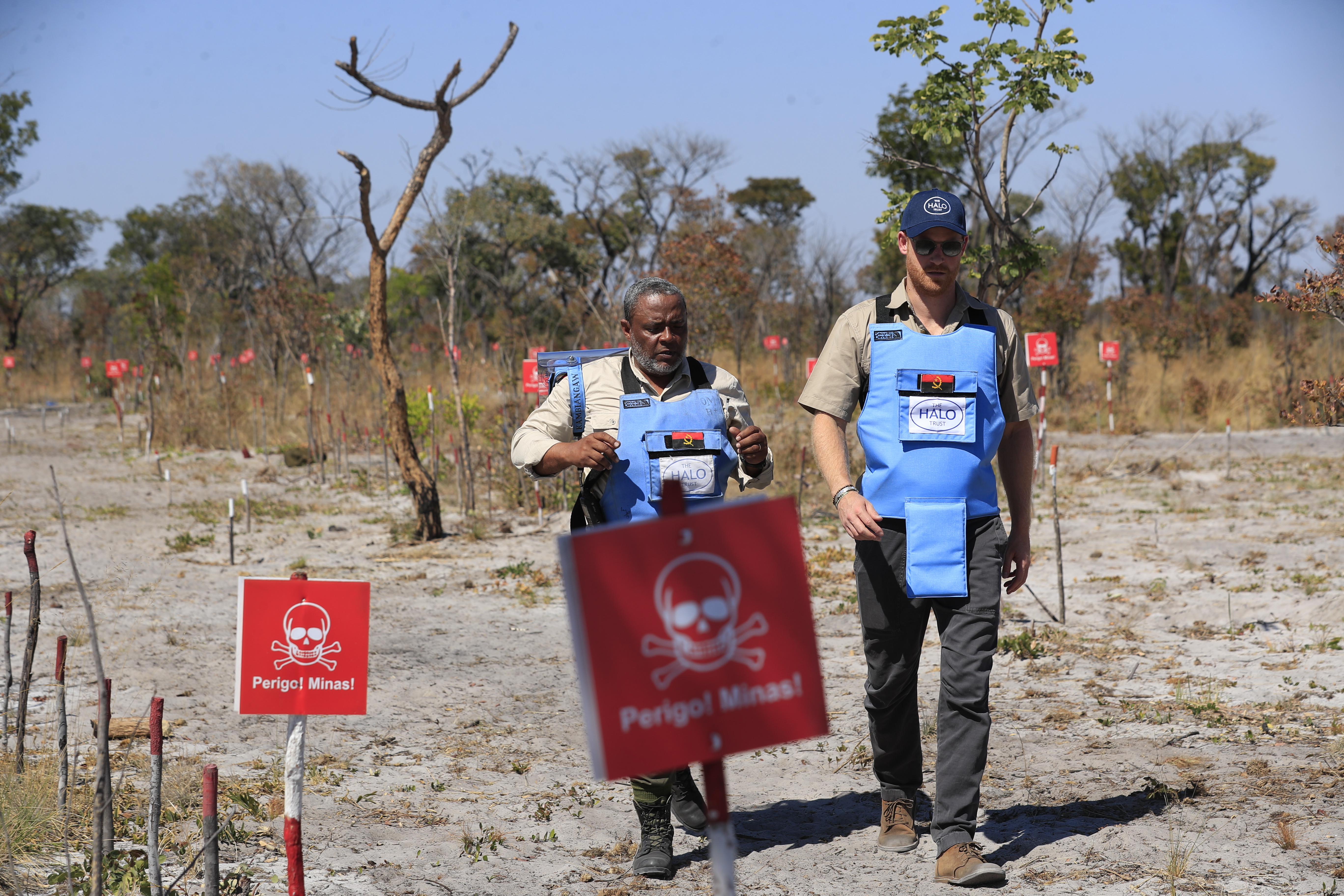 Prince Harry walking through a minefield with a man wearing a protective vest