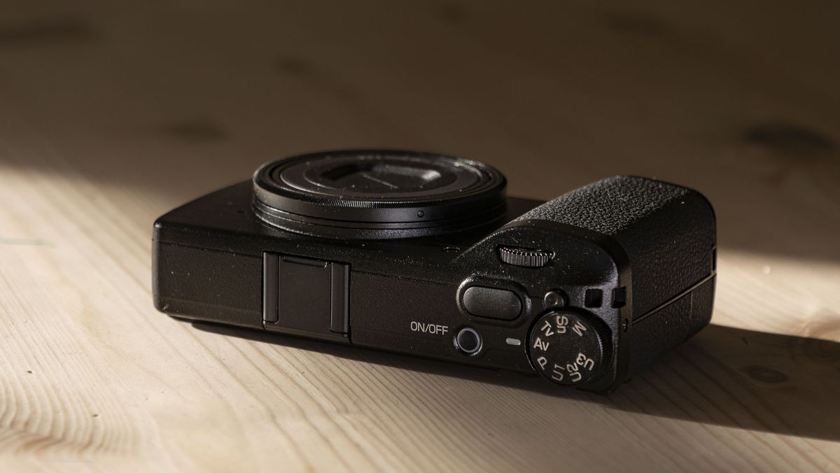 Ricoh GR IV compact camera on a wooden table, facing up, lens closeed