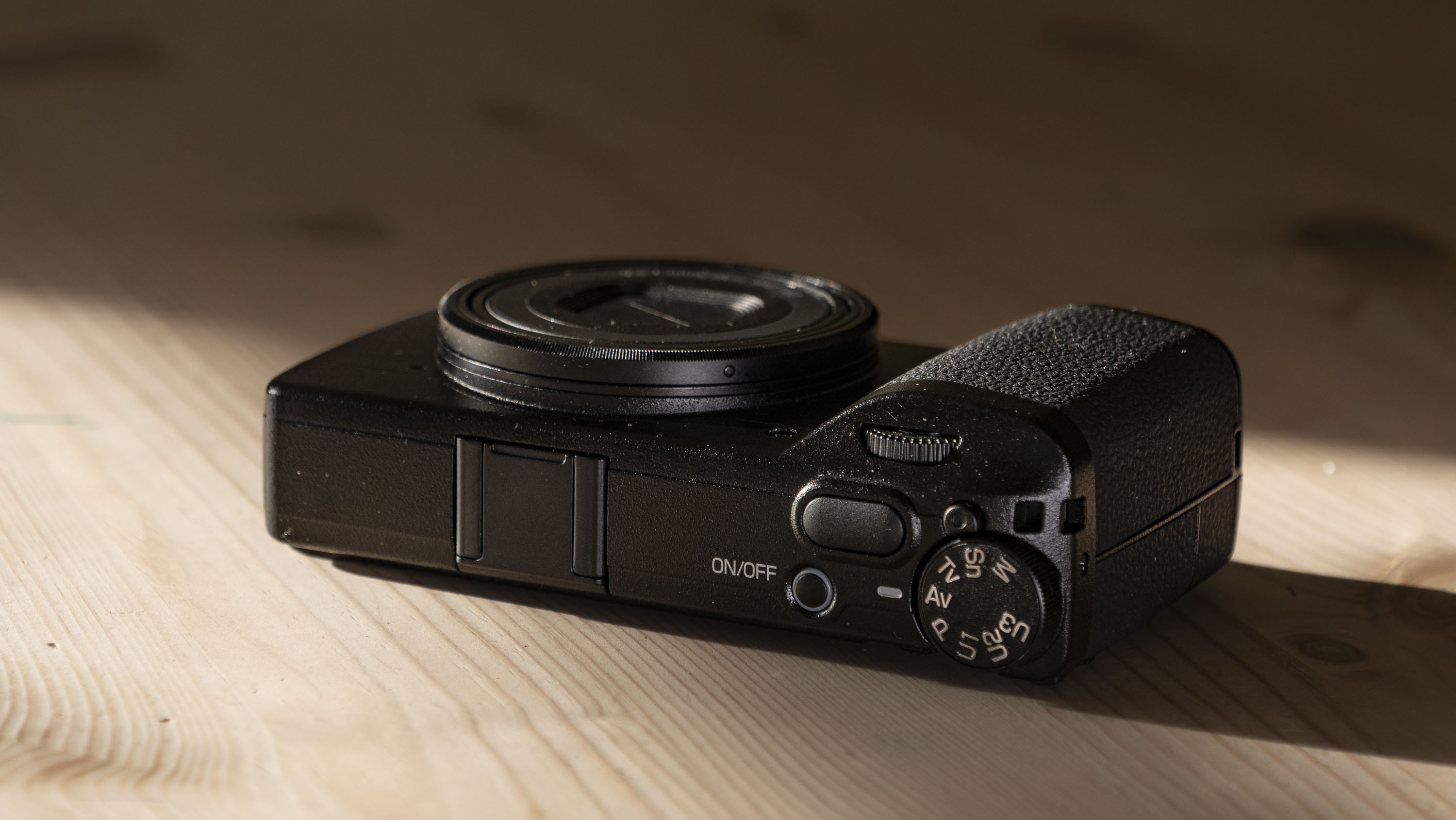 Ricoh GR IV compact camera on a wooden table, facing up, lens closeed
