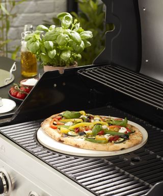 A pizza cooking on grill grates on a gas bbq