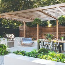 Covered outdoor kitchen area with wooden pergola, BBQ and dining area with table and chairs