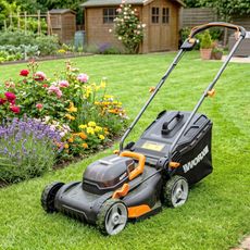 A lawn mower on grass next to a flower bed