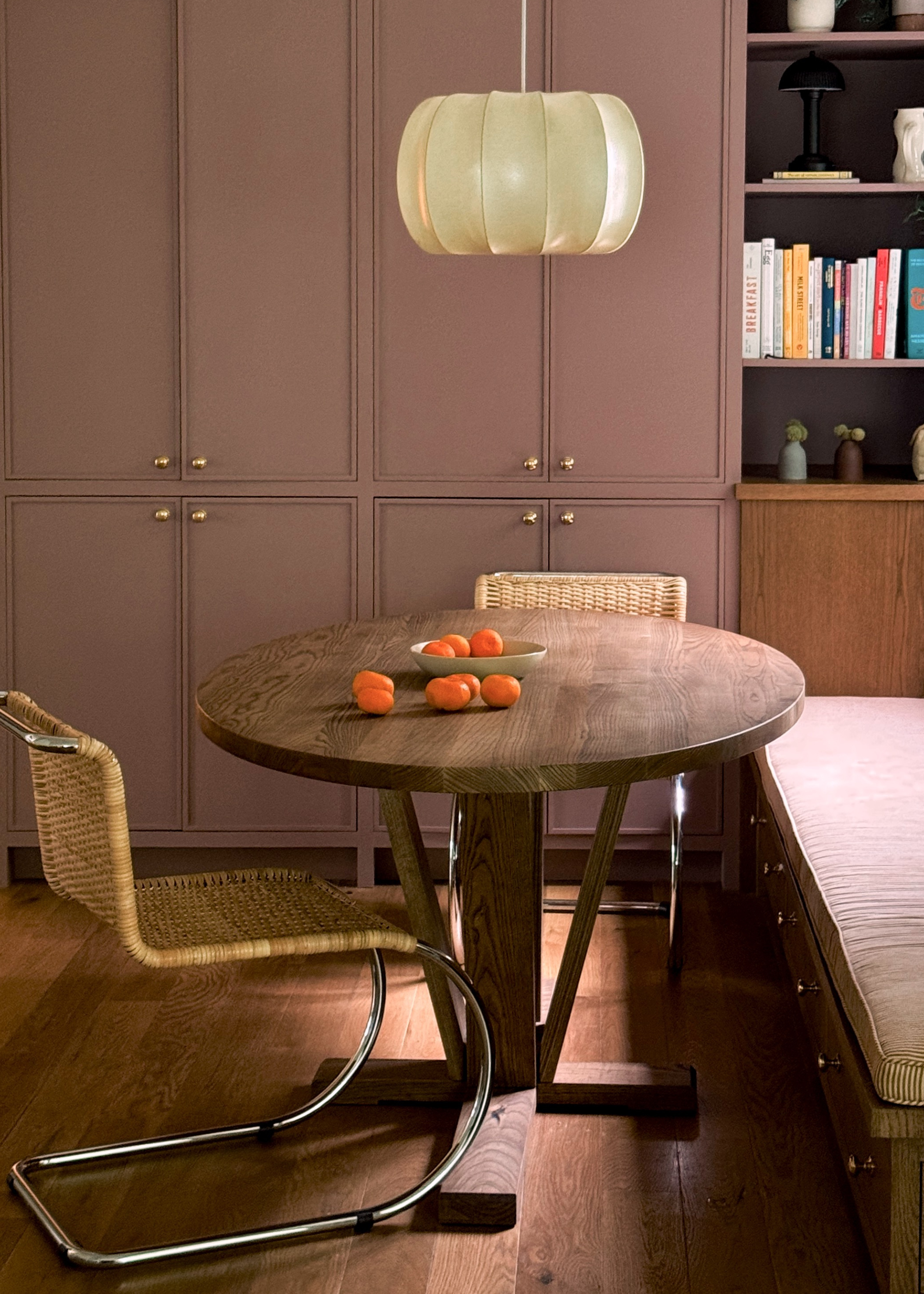 A dusty pink closet with gold handles near a seated dining nook